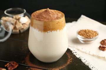 Delicious dalgona coffee in glass, granules, walnuts and brown sugar on wooden table, closeup