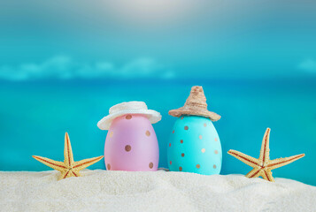 Blue and pink eggs in hats with starfish on the sand of the beach, beyond the sea. Easter in hot countries. Copy space