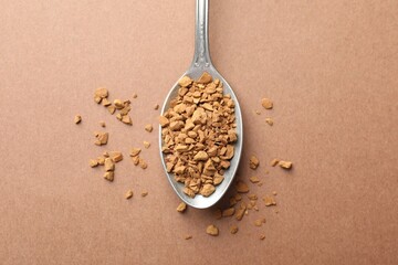 Spoon with granulated instant coffee on beige background, top view