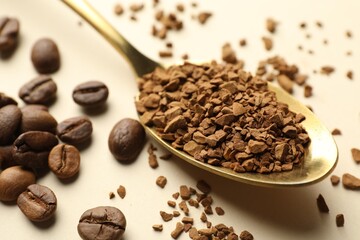 Spoon with granulated instant coffee and beans on beige background, closeup