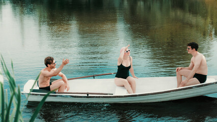 Three young adults smiling in rowboat on lake, woman looking forward in white sunglasses. Concept...