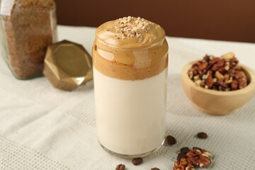Delicious dalgona coffee in glass, beans, walnuts and granules on table, closeup
