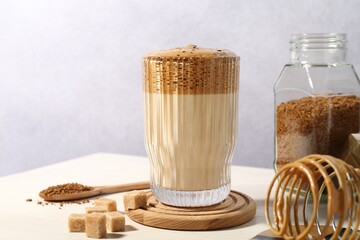 Delicious dalgona coffee in glass, whisk, brown sugar and granules on light table