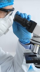 Medical scientist senior man wearing protective mask, glasses and bouffant cap using microscope doing scientific research in a laboratory. Medicine and science concept