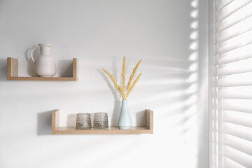 Wooden shelves with tableware and spikes in vase on white wall