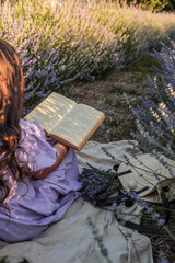 Girl in lavender dress reading a book in a blooming lavender field. Summer picnic scene with...