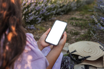 Woman in lavender field holding smartphone with blank screen. Summer picnic scene with straw hat,...