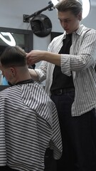 Professional barber carefully trimming customer's hair with electric clipper, providing a stylish...