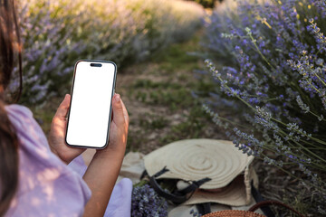 Woman in lavender field holding smartphone with blank screen. Summer picnic scene with straw hat,...