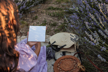 Girl holding blank white card in lavender field, wearing lilac dress. Perfect mockup for branding...