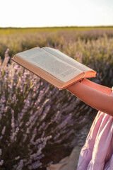 Girl in lavender field holding open book under clear sky. Warm sunlight highlights pages and purple...