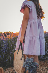 Girl in lavender field at sunset holding a straw bag with a fresh lavender bouquet. Soft light and...