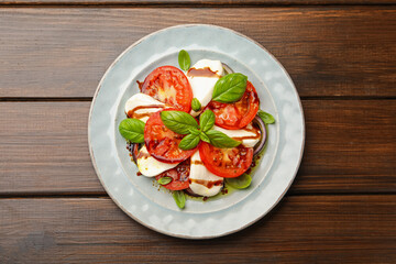 Tasty salad Caprese with mozzarella, tomatoes, basil and spices on wooden table, top view