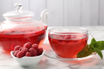 Tasty raspberry tea, berries and leaves on white marble table, closeup