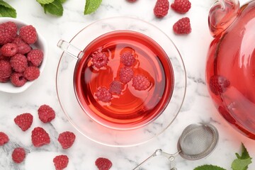 Tasty raspberry tea, berries and leaves on white marble table, flat lay