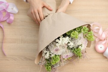 Florist making bouquet of flowers at wooden table, above view