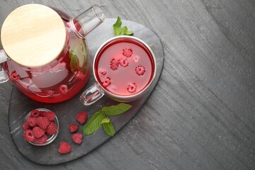 Aromatic raspberry tea in glass cup, teapot, berries and mint on black table, top view. Space for text