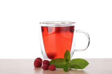 Aromatic raspberry tea in glass cup, berries and green leaves on wooden table against white...