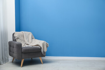 Comfortable armchair with plaid near blue wall indoors. Space for text