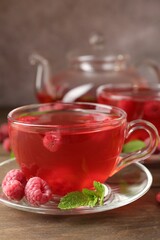 Tasty raspberry tea in glass cups, teapot, berries and mint on wooden table, closeup