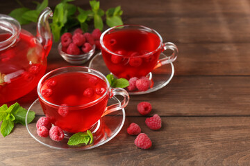 Tasty raspberry tea in glass cups, teapot, berries and mint on wooden table, closeup. Space for text