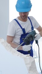 Man construction worker demolishing concrete wall with rotary hammer, wearing protective safety...