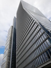 Obraz premium A modern, reflective, glass skyscraper reaching into the cloudy sky. The perfect glass reflecting the grey, dull clouds. Taken in London to show a generic skyscraper making it perfect for advertising.