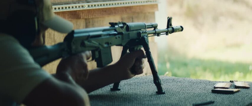 Man fires rifle with bipod as muzzle flash appears during outdoor target training at shooting range