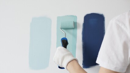 Painter wearing protective gloves rolling blue paint on white wall, creating gradient color effect...