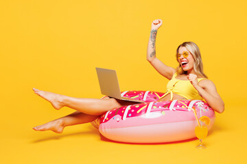 Full body young IT woman wear bikini swimsuit rest hotel pool lies on rubber ring work use laptop...