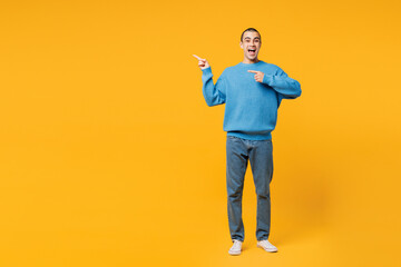 Full body young happy middle eastern man wearing blue sweatshirt casual clothes point index finger aside on area mock up isolated on plain yellow orange background studio portrait. Lifestyle concept.