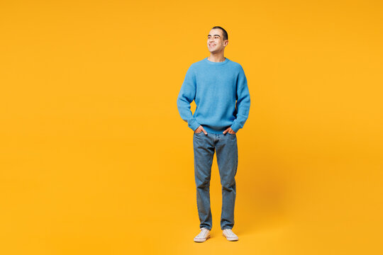 Full body young smiling happy cheerful middle eastern man wearing blue sweatshirt casual clothes stand look aside on area isolated on plain yellow orange background studio portrait. Lifestyle concept.