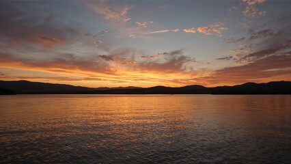 Obraz premium Bathing lake at mountain lakeshore in orange sunset sky, with mountain silhouette, wispy clouds