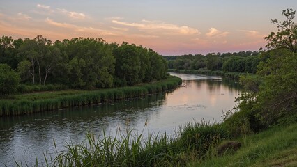 Flowing meandering river reflecting cloudy sunset sky at rural riverside with reeds and green trees