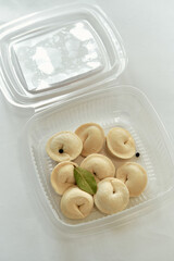 An assortment of traditional dumplings beautifully arranged in a clear plastic container, showcasing their delicate texture and inviting appearance, perfect for any culinary enthusiast.