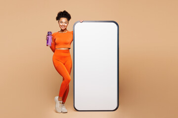 Full body young fitness trainer instructor woman wear orange clothes spend time in gym big blank...