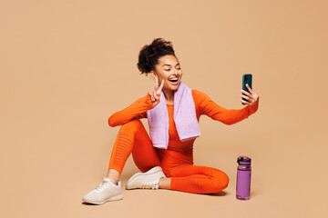 Full body young fitness trainer sporty woman sportsman in orange clothes towel spend time in gym sit do mobile cell phone selfie shot isolated on plain beige background Workout sport fit abs concept