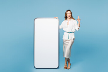 Full body young employee business woman corporate lawyer she wear shirt classic formal clothes work in office big huge blank screen mobile cell phone point finger up isolated on plain blue background.