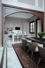 Classic interior with a wooden arch connecting the dining room, featuring a dark table and patterned rug, to the modern, bright kitchen area.