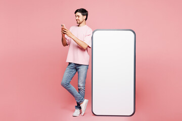 Full body young fun man wear t-shirt casual clothes big huge blank screen mobile cell phone with workspace copy space mockup area using smartphone isolated on plain pink background. Lifestyle concept.