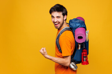 Young traveler man carry backpack with stuff mat do winner gesture isolated on plain yellow...
