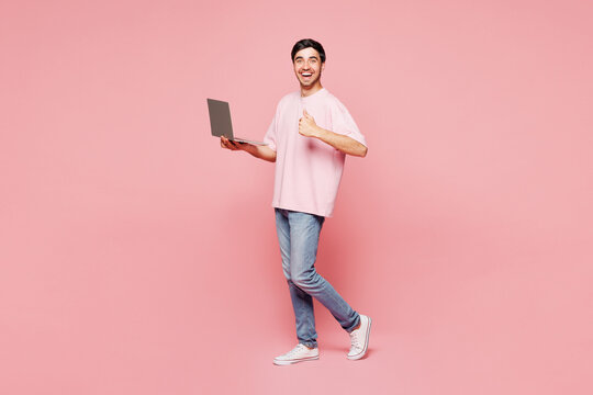 Full body side view young IT man he wearing t-shirt casual clothes hold use work on laptop pc computer show thumb up isolated on plain pastel light pink background studio portrait. Lifestyle concept.