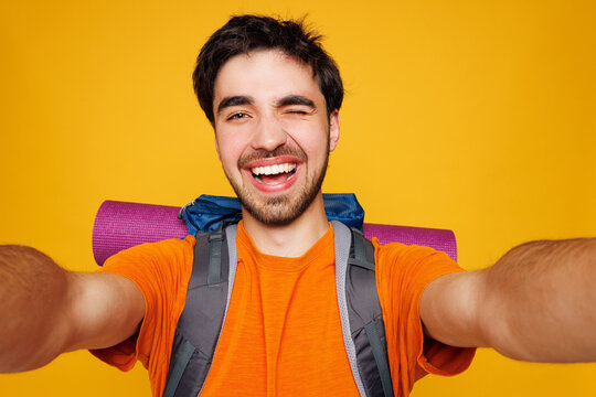 Young traveler man carry backpack with stuff mat do phone selfie wink isolated on plain yellow background Tourist lead active healthy lifestyle walk on spare time Hiking trek rest travel trip concept