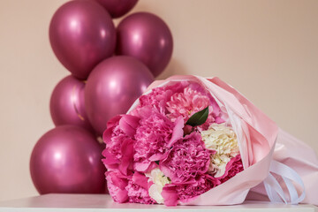 Close-up of pink and white flower bouquet wrapped in pastel paper with glossy pink balloons in the background. Bright, festive composition perfect for celebration themes