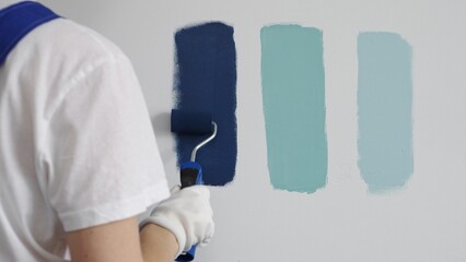 Painter wearing protective gloves rolling blue paint on white wall, creating gradient color effect...
