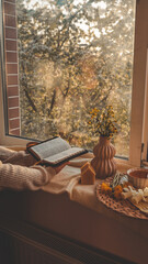 Cozy scene with a person reading a Bible by the window at sunset. Warm light, knitted blanket,...