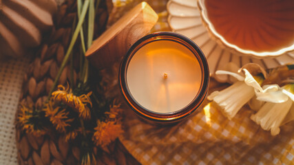Flat lay of a cup of tea, candle, and fresh spring flowers on a yellow gingham cloth in warm...