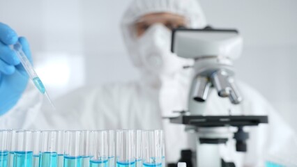 Scientific researcher wearing protective equipment, carefully pipetting liquid into test tubes...