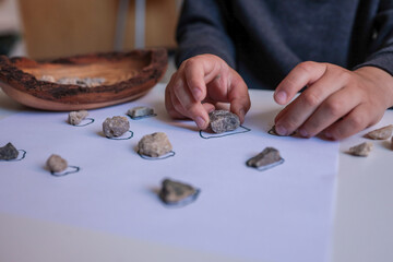 Child sorting small natural stones onto drawn circles on white paper. Educational and sensory activity promoting fine motor skills, focus, and nature-based learning at home