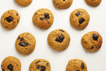 Flat lay of homemade chocolate chunk cookies on white background, arranged in a neat pattern.